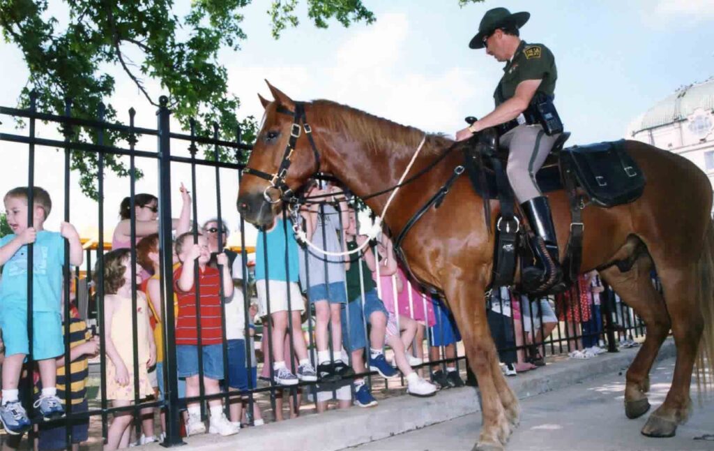 Schoolchildren line a fence to greet a mounted officer