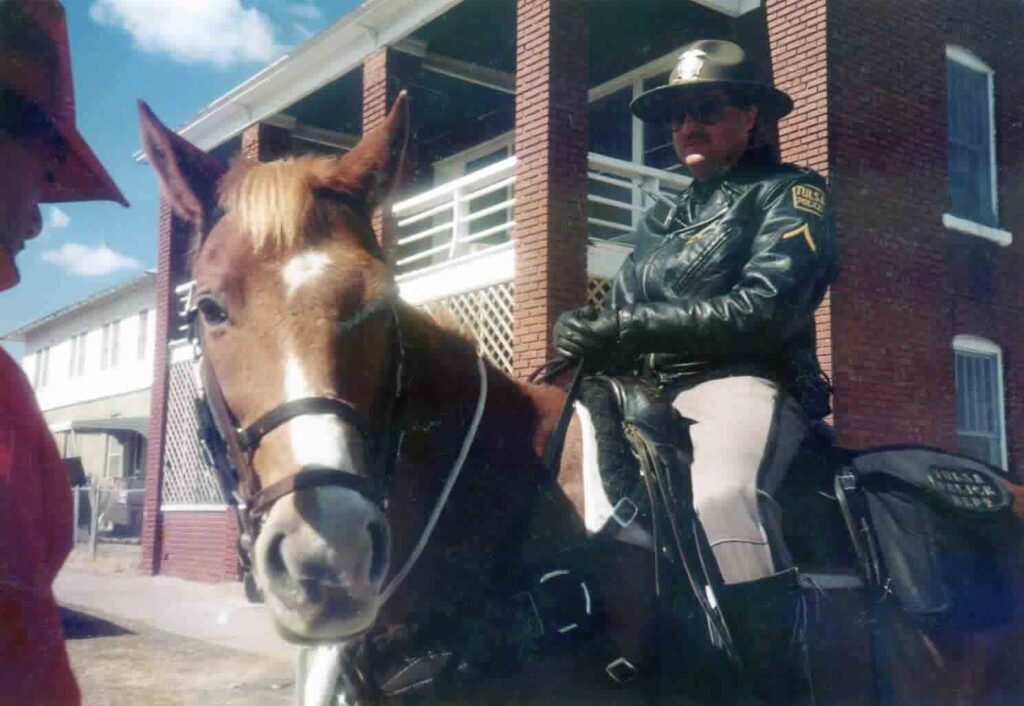 Mounted officer in a leather jacket beside a brick building