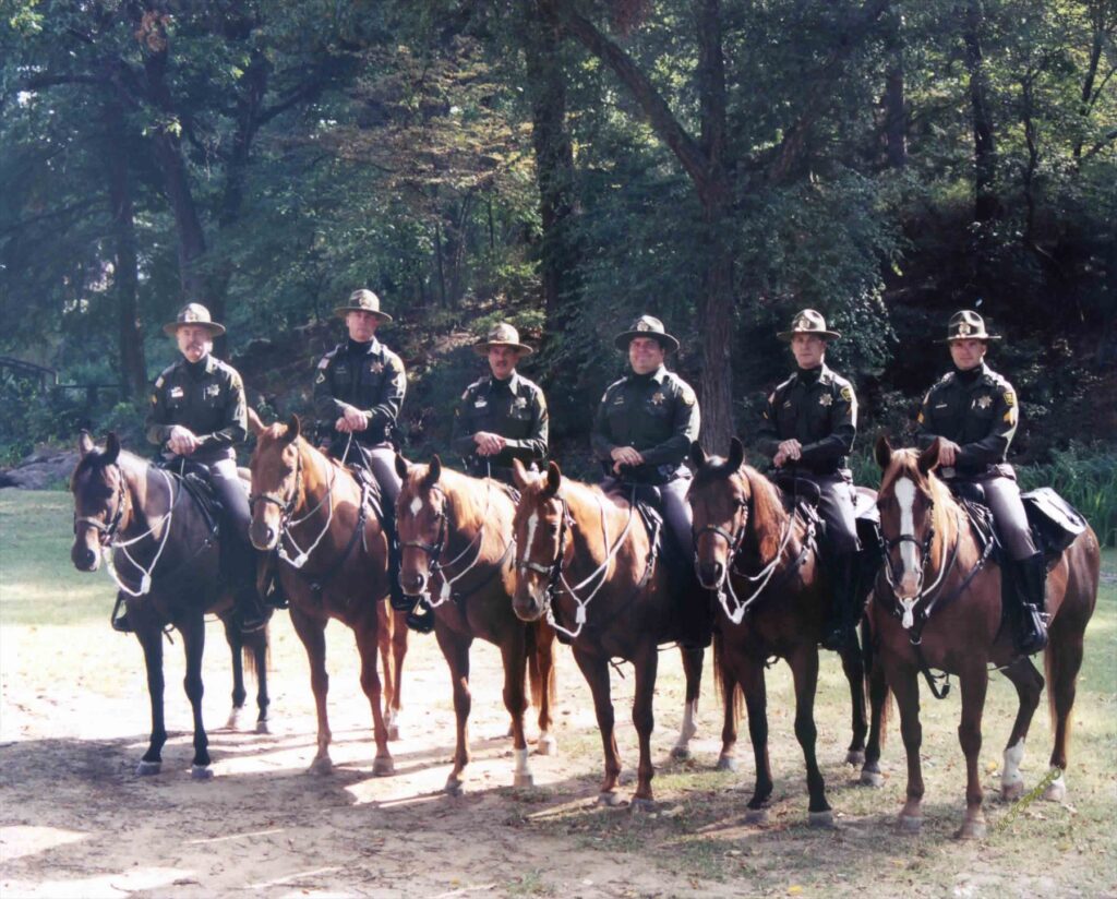 Six Tulsa mounted officers lined up on horseback under the trees