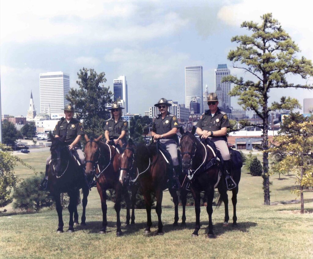 Four mounted officers on horseback in front of the downtown Tulsa skyline