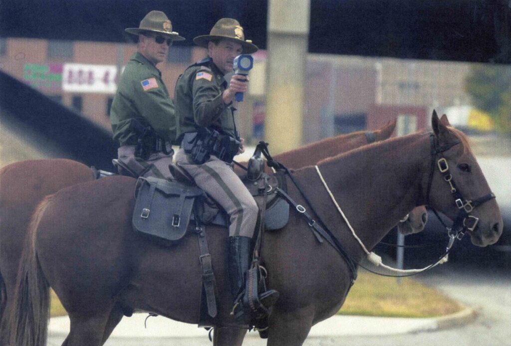 Two mounted officers, one aiming a radar gun from horseback