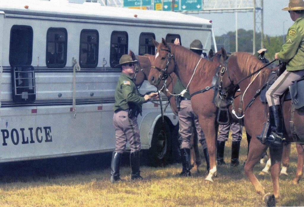 Officers and horses gather beside a white police bus