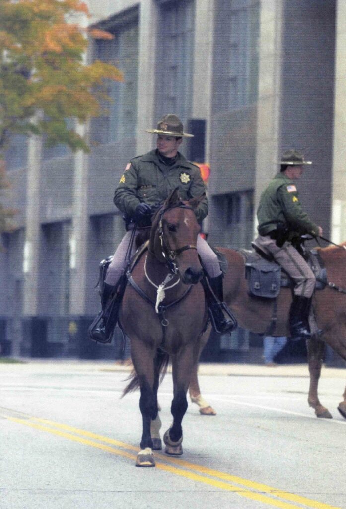 Two mounted officers ride down a downtown street