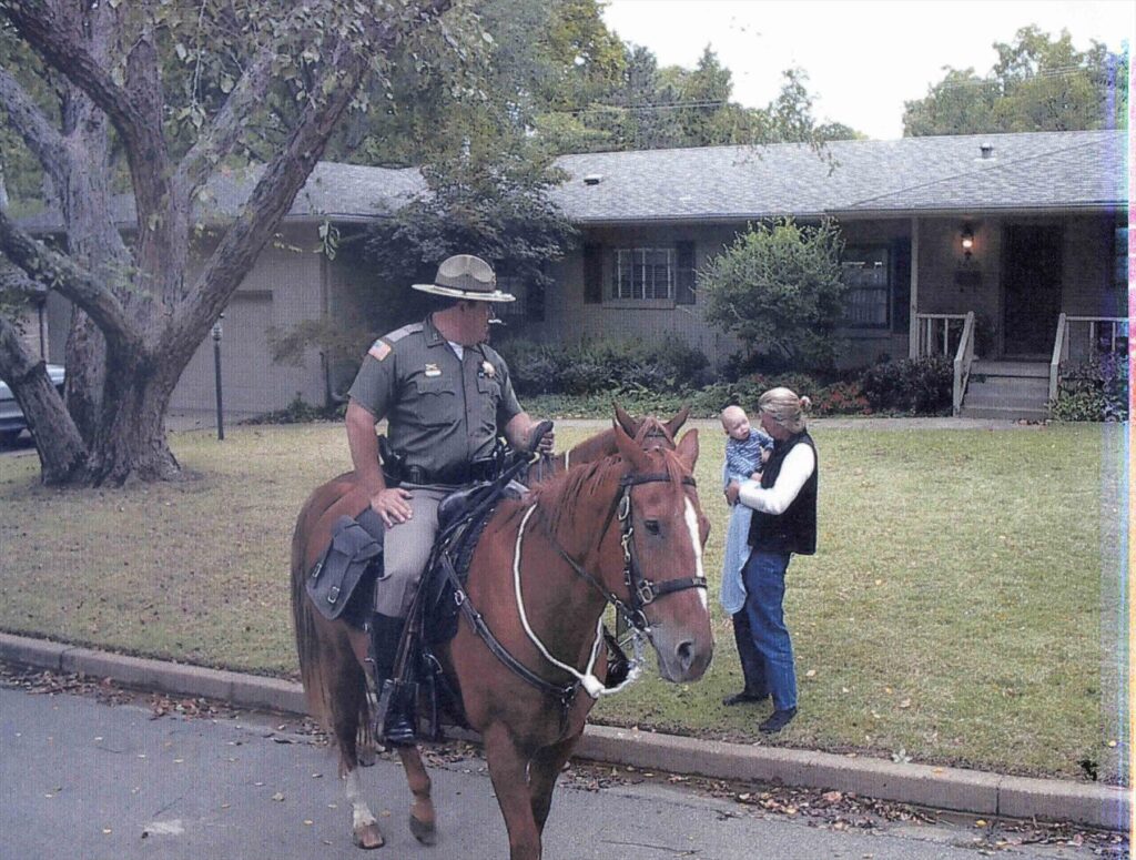 A mounted officer stops to visit with a resident holding a baby