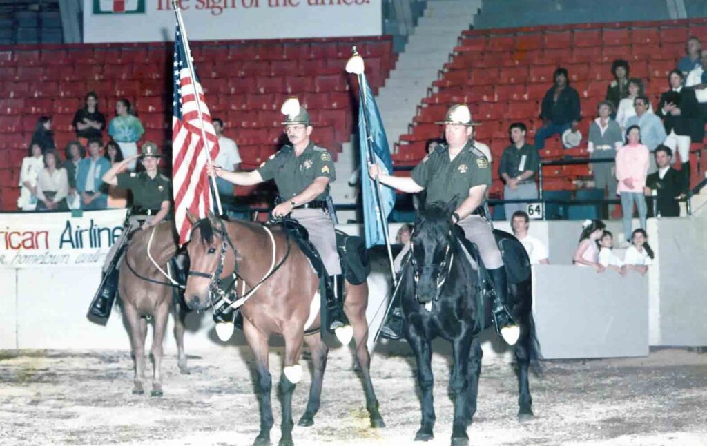 Mounted color guard carries flags in an arena in 1990